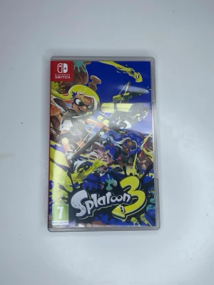 Splatoon 3 till Nintendo Switch - Splatoon 3 är ett färgstarkt och actionfyllt spel till Nintendo Switch där du slåss med bläck och tävlar i lag. Omslaget har en mix av blått, gult och svart med coola karaktärer och graffiti-inspirerad design. Perfekt för dig som gillar snabba matcher och kreativt kaos.