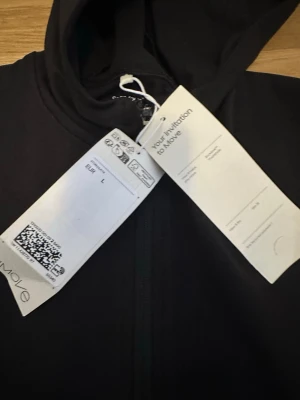 Svart träningströja från move  - Svart huvtröja med dragkedja framtill. Tröjan har långa ärmar och en huva. Det finns två fickor med dragkedja på sidorna.  Slim fit modell, kort i modellen, står L men motsvarar en M :) cirka 55 cm lång och cirka 67 cm i ärmarn