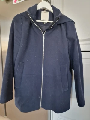 Mörkblå jacka från Esprit - Mörkblå jacka från Esprit med dragkedja framtill och två fickor. Snygg huva och enkel design som funkar till det mesta.