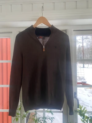 Mörk grå tröja från Morris - Snygg mörk grå  stickad tröja från Morris med halv dragkedja och diskret broderad logga på bröstet. Tröjan har ribbade muddar vid ärmslut och nederkant, perfekt för lager på lager. Materialet känns mjukt och bekvämt.