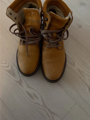 Bruna fodrade kängor med grov sula - Säljer ett par bruna kängor med snörning och grov sula. Kängorna har ett varmt, ljust foder och detaljer i metall vid snörningen. Perfekta för kalla dagar och outdoor-stil. Materialet är mocka eller nubuck och de har rejäla snören i kontrastfärg. Endast använda en gång💕