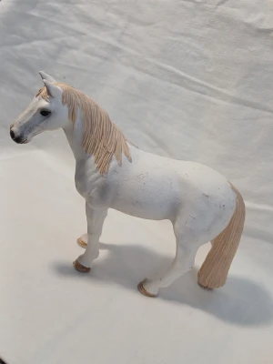Vit hästfigur i plast. Fabrikat Schleich. - Säljer en vit hästfigur i plast med ljusbrun man och svans. Figuren har realistiska detaljer och står stadigt på fyra ben. Perfekt som dekoration eller leksak för dig som gillar djur och hästar.