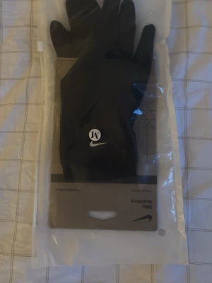 Svarta Nike Therma-Fit handskar - Snygga svarta Nike Therma-Fit handskar. Har en smidig passform som passar perfekt för utomhusträning under kyligare dagar. Handskarna har även touch screen på tummen och pekfingret!