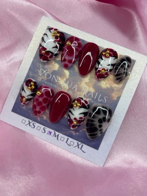 CherrySafari (M);Short Almond - Unika press-on naglar i mandelform från Von Juan Nails. Setet har vinröda, svartvita och transparenta naglar med coola mönster, guldfärgade detaljer och handmålad design. Perfekt för dig som vill sticka ut med trendiga och kreativa naglar.