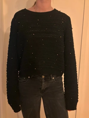 Svart stickad tröja med pärlor - Säljer en svart stickad tröja med dekorativa små pärlor över hela tröjan. Tröjan har rund halsringning, lång ärm och en något boxig passform. Perfekt för dig som vill ha en enkel men ändå unik look.