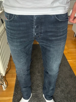 Mörkblå slim fit jeans herr - Snygga Diesel Tepphar i mörkblå tvätt med perfekt fade! Modern klassiker med knappgylf och snygga slitningsdetaljer. Bekväm passform. 🧵 Märke & Modell: Diesel - Tepphar 📏 Storlek & Passform: W32, SlimCarrot (rymligare upptill, avsmakande nedtill) 📐 Mått A: 43 B: 75 C: 103 cm ✅ Skick: 7/10. Naturlig fade, patch bak saknas. ✨ Detaljer: Knappgylf, Diesel Industry-logga på myntficka, märken bak. 💰 Nypris ca 1500 kr 🧍 Referens: passar ca 181-186 cm ‼️ Skickas samma dag/dagen efter ‼️