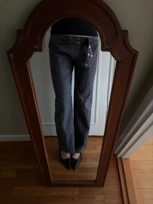 Linnebyxor - Säljer ett par grå kritstrecksrandiga linnebyxor. Byxorna har raka ben och en unik knäppning med flera silverfärgade knappar framtill samt en silverfärgad bältesring som möjliggör en rad olika knäppningar.