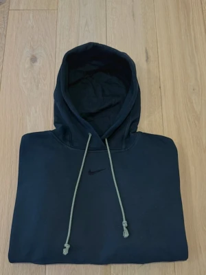 Mörkgrön hoodie från Nike med logga - Snygg mörkgrön hoodie från Nike med diskret svart broderad logga på bröstet. Hoodien har en klassisk känguruficka framtill och dragsnören i huvan. Tillverkad i mjukt bomullsmaterial och har ribbade muddar vid ärmslut och nederkant.