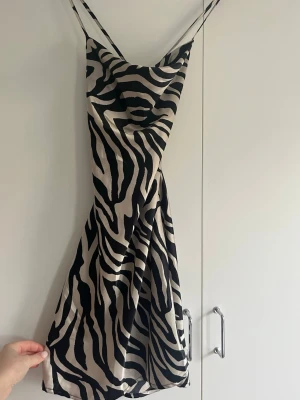 Zebramönstrad kort siden klänning - Säljer en snygg kort klänning i siden med zebramönster. Klänningen har tunna axelband som korsas i ryggen och en öppen rygg.