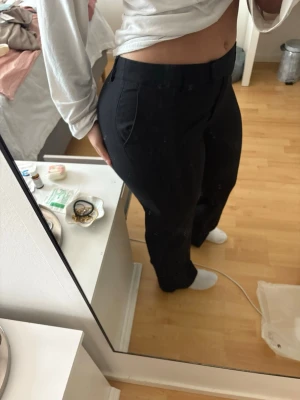 Svarta kostymbyxor i linne - Säljer ett par svarta kostymbyxor med raka ben och hög midja. Byxorna har diskreta fickor på sidorna och hällor för skärp. Klassisk och stilren modell som passar till många olika looks. Materialet ser ut att vara en mjuk och följsam blandning, perfekt för en clean outfit. Linnemix. Nypris 500kr