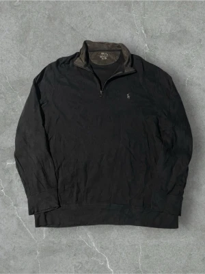 Marinblå halvzip från Polo Ralph Lauren | XL - Klassisk marinblå långärmad tröja från Polo Ralph Lauren med halv dragkedja och liten broderad logga på bröstet. Tröjan har hög krage och är tillverkad i mjukt bomullsmaterial. Perfekt för en avslappnad men stilren look.