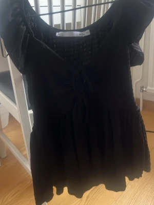 Svart tunt  linne - Söt svart tröja med rosset framtill och volangdetaljer vid axlarna. 