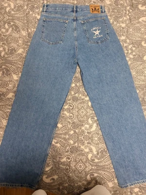 Blå raka baggy jeans Sweet Skies - Säljer ett par ljusblå raka jeans från Sweet Skies med klassisk femficksmodell. Jeansen har en broderad detalj på ena bakfickan och en läderpatch i midjan. Tillverkade i denim med en avslappnad passform och hög midja.