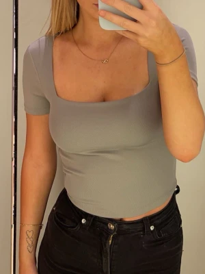 Grå croppad topp med fyrkantig ringning - Snygg grå croppad topp från New Yorker med fyrkantig ringning och korta ärmar. Tillverkad i mjuk och stretchig bomullsblandning som sitter tight och framhäver figuren. Perfekt att matcha med höga jeans eller kjol. Använd några fåtal gånger.🩶 Storlek S