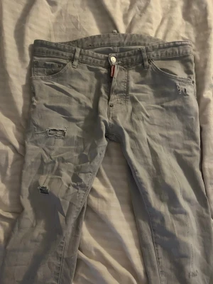 Gråa slitna jeans från Dsquared2 - Säljer ett par gråa jeans från Dsquared2 med slitna detaljer och klassisk femficksmodell. Jeansen har en rak passform och är tillverkade i mjuk bomull. Perfekta för dig som gillar en avslappnad och trendig stil.