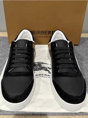 Burberry svarta sneakers med rutigt - Snygga svarta sneakers från Burberry med klassiskt rutigt mönster på hälen. Skorna har en låg profil, vita sulor och svarta skosnören. Materialmix av läder och mocka ger en lyxig känsla. Perfekt för dig som vill ha en stilren och trendig look.Kom dm för eventuella frågor 🧐pris kan alltid diskuteras 😊