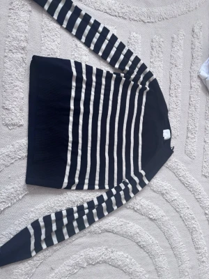 Svart och vit randig stickad tröja - Snygg stickad tröja med svarta och vita horisontella ränder. Tröjan har långa ärmar och rund halsringning. Materialet känns mjukt och stretchigt, perfekt för en avslappnad look. Klassisk design som passar till jeans eller kjol. 