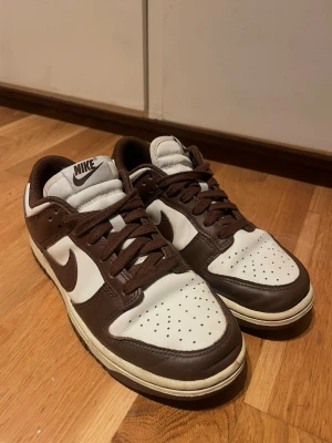 Nike Dunk Low brun och vit - snygga Nike Dunk Low i brun/vit färg  storlek 37.5  använda men fortfarande i bra skick (se bilder) 🤎  säljer då de inte används #nike #dunks #nikedunk #sneakers #brun #streetstyle #37