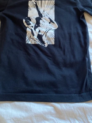 Jordan svart - Cool svart t-shirt med ett stort vitt manga-inspirerat tryck på framsidan som föreställer en actionfylld karaktär. Klassisk passform och korta ärmar. Perfekt för dig som gillar streetstyle och anime-vibes.