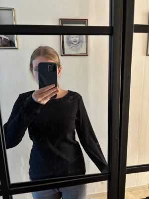 Svart långärmad topp med öppen rygg - Svart långärmad topp med rund halsringning och snygga korsade band i ryggen som ger en öppen rygg-effekt. Perfekt för dig som gillar stilrena plagg med en twist. Mjuk och stretchig känsla.