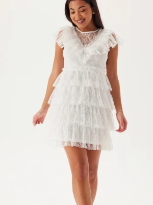 Vit spetsklänning med volanger - Superfin vit kortklänning i spets med flera lager volanger och transparenta detaljer upptill. Klänningen har korta ärmar och v-ringad rygg. Köpt för 899 och är i bra skick. Perfekt som studentklänning.