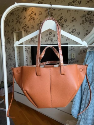 Brun fin handväska - En wsuper fin brun väska, köpt från amazon och är märket Acuye. Är helt ny, all plast är kvar så är helt ny. Väskan går att göra till två väskor som ses på bilden där man kan vika in kanterna. Ingår även en liten clutch som är med. Är två olika längd på axelband beroende på hur man vill ha den. Måtten på den är 42x25x8,5cm. Säljs då jag glömde skicka tillbaka innan returtiden, är inte min stil.