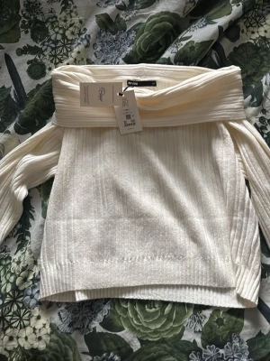 Off shoulder vit tröja från Bik Bok - Trendig off shoulder-tröja från Bik Bok i mjukt, ribbstickat material. Färgen är klassiskt vit och modellen har långa ärmar och bred krage som vilar över axlarna. Perfekt för en stilren och modern look. HELT NY! Fick två så säljer den ena 🥰🫶🏼🩷