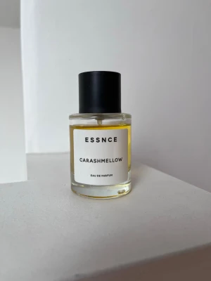 ESSNCE Carashmellow Eau de Parfum - ESSNCE Carashmellow Eau de Parfum i en stilren, rund glasflaska med svart lock. Parfymen har en ljusgul vätska och minimalistisk etikett. Flaskan är kompakt och enkel att ta med sig. Perfekt för dig som gillar unika dofter och snygg design.