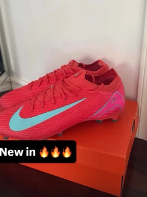 Nike Mercurial röda fotbollsskor - Säljer ett par Nike Mercurial fotbollsskor i en riktigt snygg röd färg med turkosblå swoosh och detaljer. Skorna har låg profil, snörning och är tillverkade i ett lätt syntetmaterial för bästa bollkontroll och grepp på planen. Perfekta för dig som vill sticka ut på matchen! PRO 