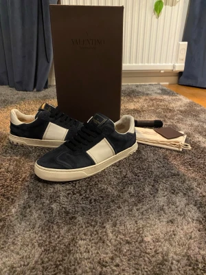 Valentino Garavani  - Snygga Valentino Garavani i mörkblå mocka och vitt läder. Lite använda men jätte Bra skick med alla nitar kvar.  Skorna kommer med original box,dustbag, extra skosnören. Storlek 40 1/2 men passar även 41 och 42