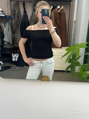 Svart offshoulder topp - Säljer en svart offshoulder topp med smockad, åtsittande passform. Toppen är croppad och har en vågig kant upptill och nedtill. Perfekt för dig som gillar en trendig och stilren look.
