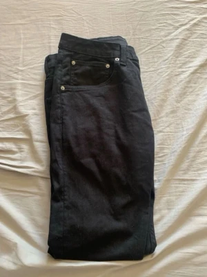 Svarta raka jeans med nitar - Säljer ett par svarta jeans med raka ben och silverfärgade nitar vid fickorna. Klassisk femficksmodell och svart patch bak i midjan. Jeansen har en stilren look och passar perfekt till en avslappnad outfit.