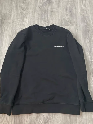 Burberry hoodie - Svart hoodie från Burberry med diskret broderad logga framtill och stor vit grafisk design på ryggen. Klassisk passform med rund halsringning och ribbade muddar. Tillverkad i mjuk bomullsblandning för maximal komfort.