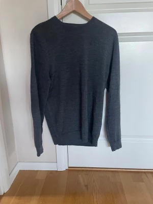 Mörkgrå merinoulltröja Dressmann - Snygg och stilren mörkgrå stickad tröja från Dressmann i mjuk merinoull. Tröjan har rund halsringning och långa ärmar, perfekt för lager-på-lager och enkel att matcha med olika outfits.