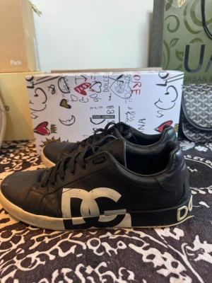 Dolce & Gabbana svarta sneakers - Svarta sneakers från Dolce & Gabbana i läder med tydlig logga i vitt på hälen och sula. Klassisk låg modell med svarta skosnören och vit yttersula med präglad logotyp. Snygg och stilren design som sticker ut med märkets ikoniska detaljer.