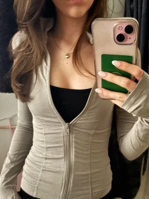 Beige tränings ziphoodie med tumhål - Snygg beige ziphoodie med figurnära passform och tumhål i ärmarna. Dragkedja framtill, Perfekt för en avslappnad och sportig look. Materialet känns mjukt och stretchigt.