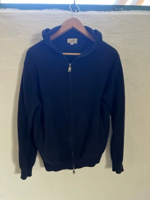 Mörkblå Kashmir zip  - Mörkblå hoodie från S&T clothing med dragkedja framtill och två fickor. Klassisk modell med huva och ribbade muddar vid ärmslut och nederkant. Tillverkad i mjukt material som känns skönt mot huden. Perfekt för en avslappnad och stilren look. Sytt ihop lite hål vid luvan 