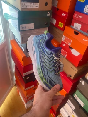 Blå Hoka One One sneakers med snörning - Snygga blå sneakers från Hoka One One med gröna och mörkblå detaljer. Skorna har en chunky vit sula och smart snörning med dragsko. Ovandelen är i mesh för bra andningsförmåga och komfort. Perfekta för dig som gillar sportig stil.