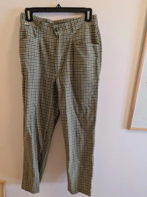 Rutiga gröna chinos med hög midja - Snygga chinos med grönt och vitt rutmönster, raka ben och hög midja. Byxorna har framfickor och stängs med knapp och dragkedja. Perfekta för dig som gillar en avslappnad men trendig stil.