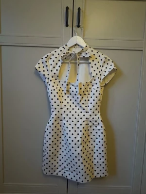 Vit miniklänning med svarta prickar Zara - Supersöt vit miniklänning med svarta prickar och knytband i halsen. Klänningen har korta ärmar, markerad midja och en snygg fyrkantig urringning. Perfekt för dig som gillar retrostil och vill sticka ut lite extra.