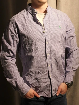 Blårutig skjorta från Polo Ralph Lauren - Säljer en klassisk blårutig skjorta från Polo Ralph Lauren med button-down krage och grönt broderat logomärke på bröstet. Skjortan har långa ärmar och vita knappar, perfekt för dig som gillar stilrena och tidlösa plagg.