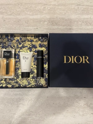 Dior Homme parfymset 100ml - Lyxigt parfymset från Dior Homme med en elegant glasflaska med amberfärgad parfym, en vit tub med svart kork för shower gel och en svart cylinderformad deodorant. Allt levereras i en mörkblå presentask med gulddetaljer och Dior-logga. Nypris ca 1500kr