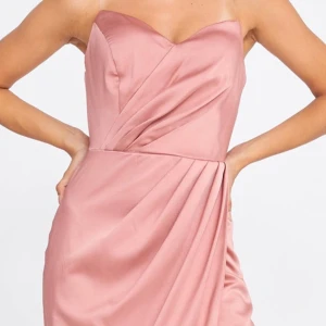 Satin rosa klänning - Köpt för 1500! Supersnygg axelbandslös långklänning i satin tyg, perfekt till bal, bröllop eller fest. Den sitter jättefint på kroppen och har en draperad midja och en liten slits fram. Bara använd en gång.