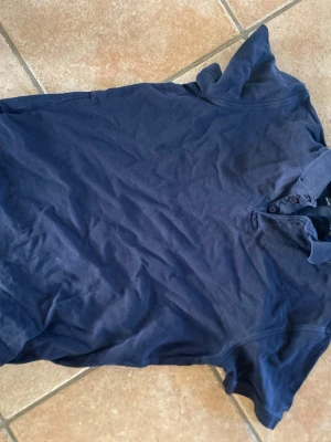 Mörkblå piké t-shirt 157 - Mörkblå piké t-shirt från 157 med klassisk krage och knappar vid halsen. T-shirten har korta ärmar och är tillverkad i mjuk bomull som känns skön mot huden. Enkel och stilren modell som passar till det mesta. Skrynklig på bilden stryker självklart innan köp.