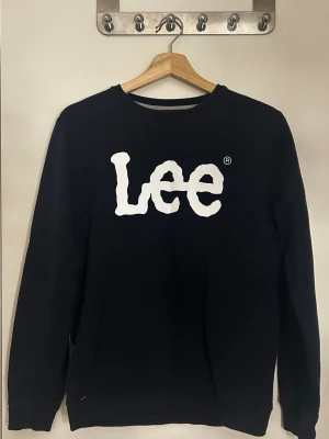 Svart sweatshirt från Lee - Cool svart sweatshirt från Lee med stort vitt logotryck på bröstet. Tröjan har rund halsringning och långa ärmar. Materialet är mjukt och bekvämt, perfekt för en avslappnad look. Passar dig som gillar klassiska streetwear-vibes.