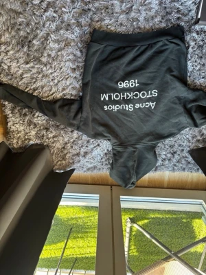 Svart hoodie från Acne Studios - Snygg svart hoodie från Acne Studios med vit text på ryggen: 'Acne Studios STOCKHOLM 1996'. Klassisk passform med huva och långa ärmar. Perfekt för en avslappnad och trendig stil.