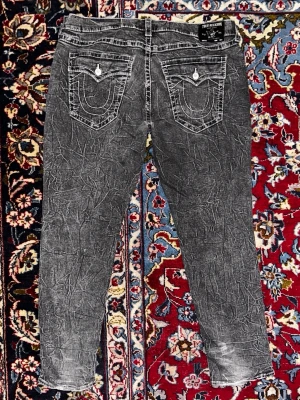 Unika True Religion jeans - Riktigt snygga gråa true religion jeans med unikt wash-pattern. Slitna i hälarna men annars bra skick. Bredd: 58cm. Längd: 116cm. Det är bara att skriva om du vill ha fler bilder eller mått.