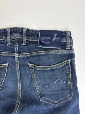 Blå jeans från Jacob Cohen - Snygga blå jeans från Jacob Cohen med klassisk femficksmodell och kontrastsömmar. Jeansen har rak passform och är tillverkade i mjukt denimtyg. Perfekta för dig som gillar stilrena och tidlösa plagg.