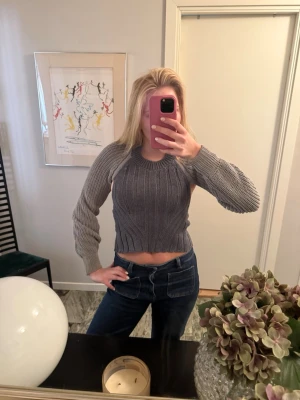 Grå croppad stickad topp - Säljer en grå croppad stickad topp med långärmad design och ribbade detaljer. Toppen har en tajt passform i midjan och är perfekt för dig som gillar trendiga och bekväma plagg. Inga synliga märken på plagget.