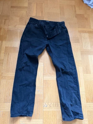 Svarta jeans från Jack & Jones - Säljer ett par svarta jeans från Jack & Jones med klassisk femficksmodell och raka ben. Jeansen har knappgylf och är tillverkade i ett mjukt denimtyg som känns bekvämt. Perfekta för en avslappnad och stilren look. Väll använda men inga direkta skavanker, skriv vid frågor☺️